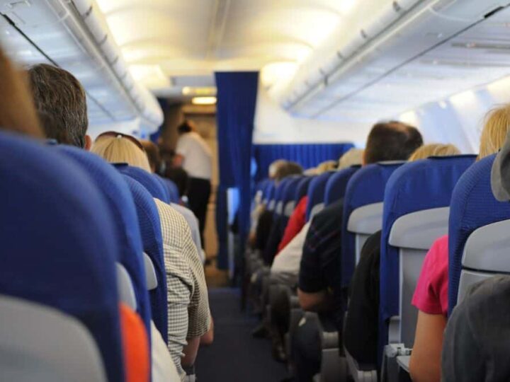 Passengers seated on an airplane, view from the back of the cabin.