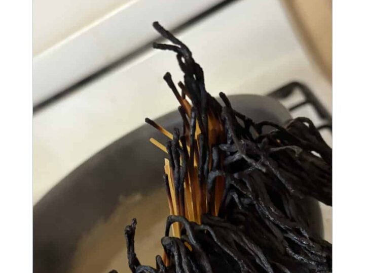 Spaghetti with blackened, burnt appearance on skewers over a pot.