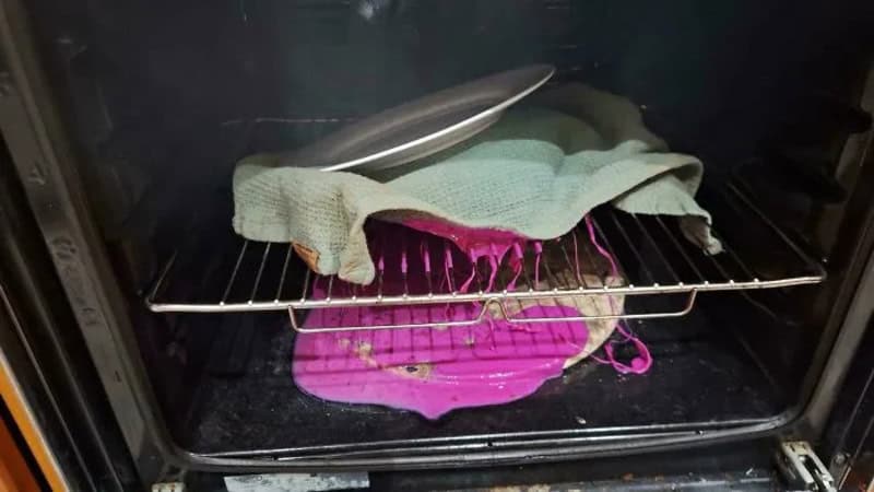 Oven with a pink liquid spill and cloth on top, no food inside.