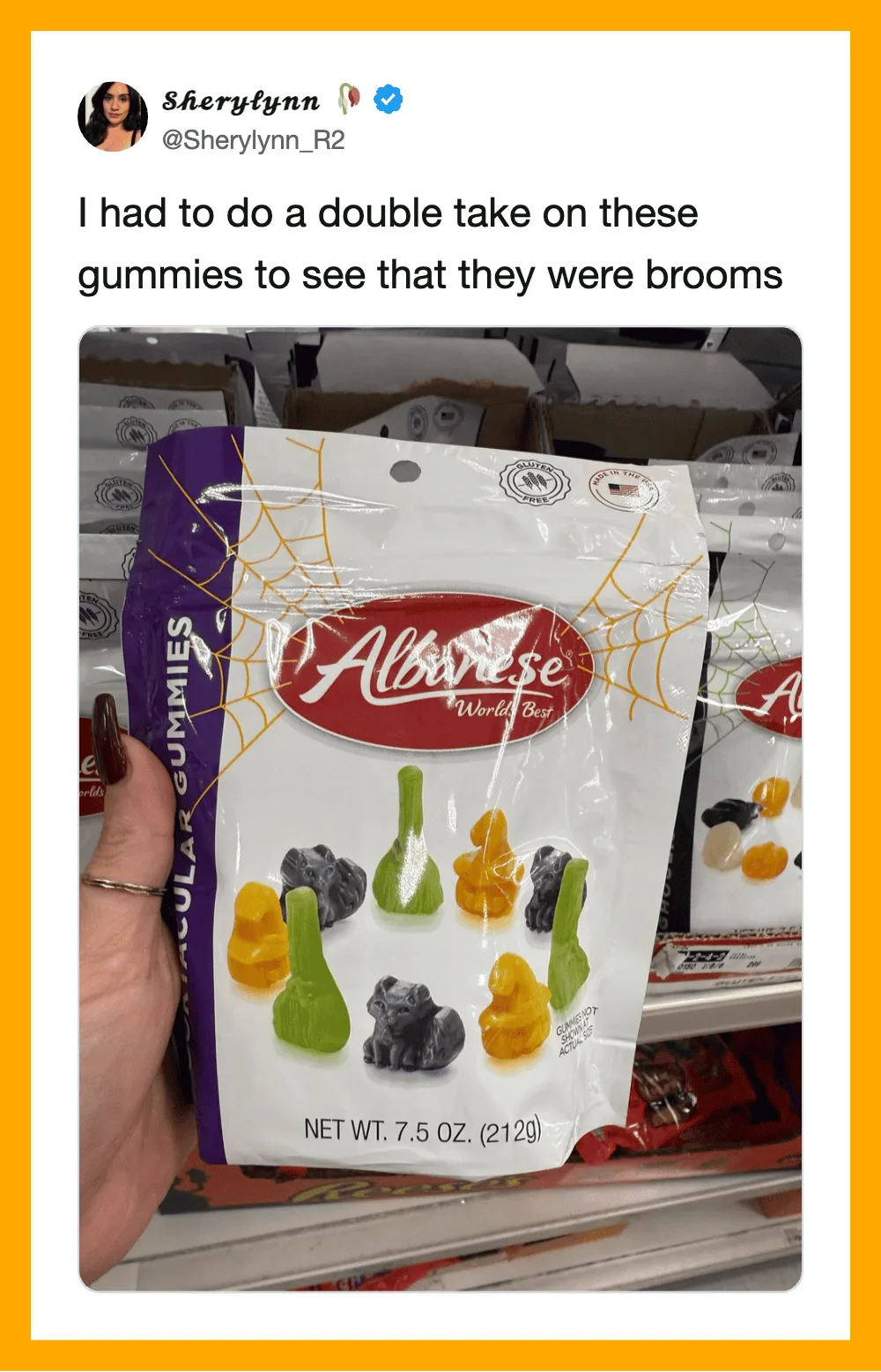 Person holding a bag of gummy candies shaped like brooms, with a store shelf in the background.