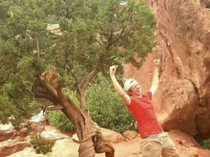 Person in red shirt and beige shorts pretending to hold a large boulder.
