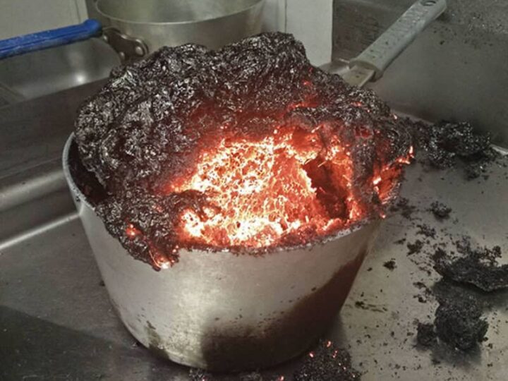 Burnt pot with charred contents and glowing embers, on a kitchen stove.