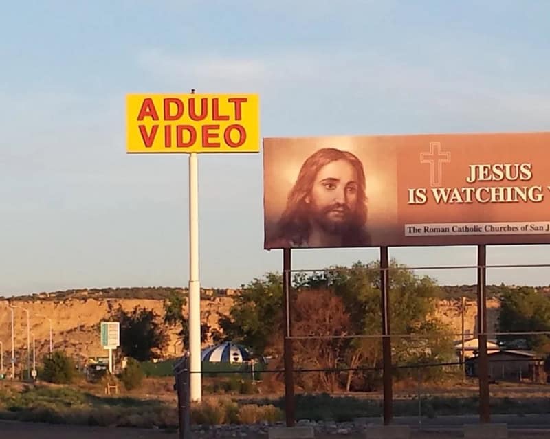 Billboard with 'ADULT VIDEO' sign and Jesus image with text 'JESUS IS WATCHING'.