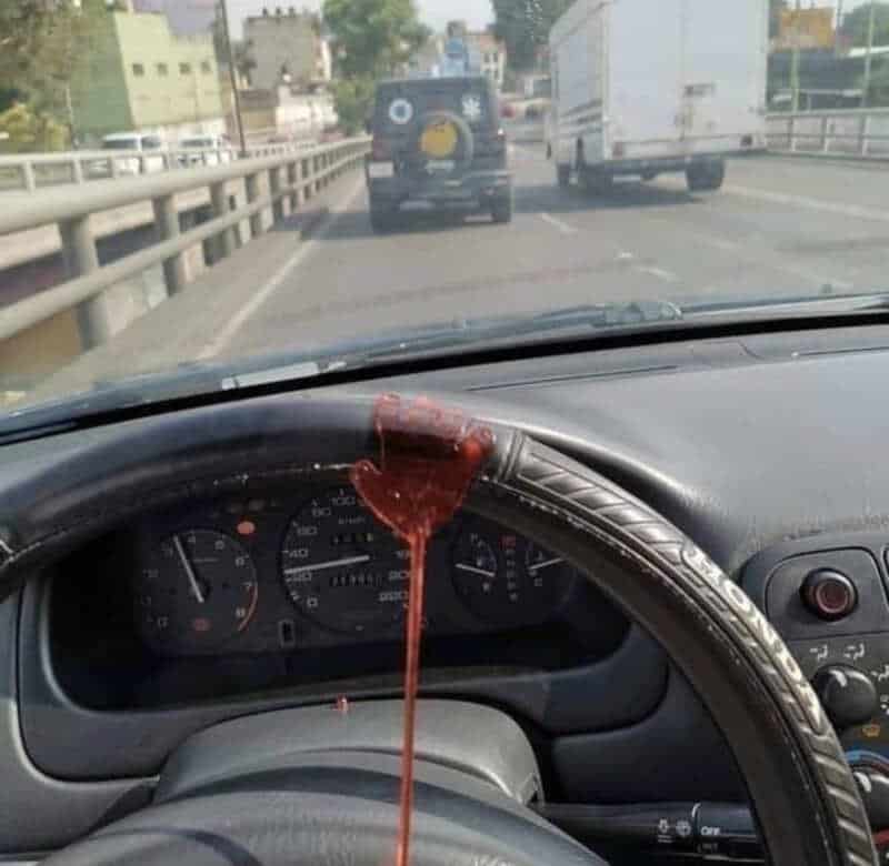 Car dashboard with red liquid spilling from the steering wheel onto the dashboard.
