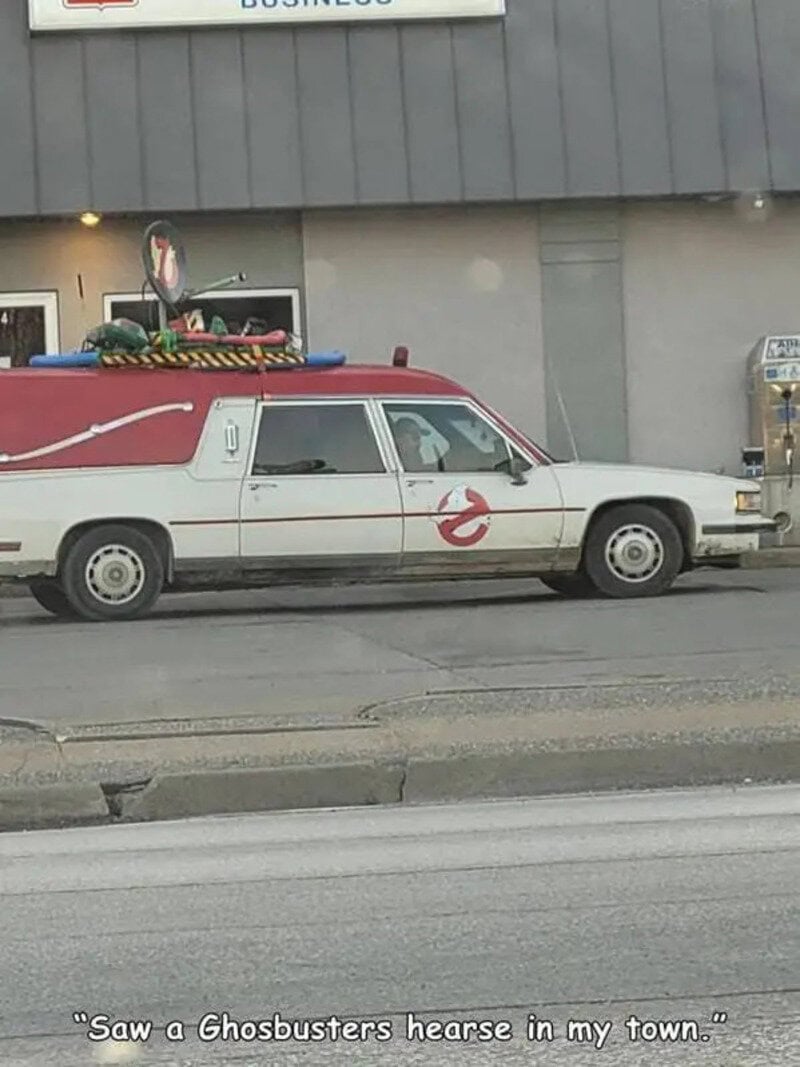 Ghostbusters hearse parked outside a building with a 'Business' sign.