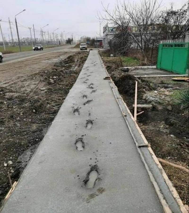 Footprints on a freshly poured sidewalk with construction tools nearby.