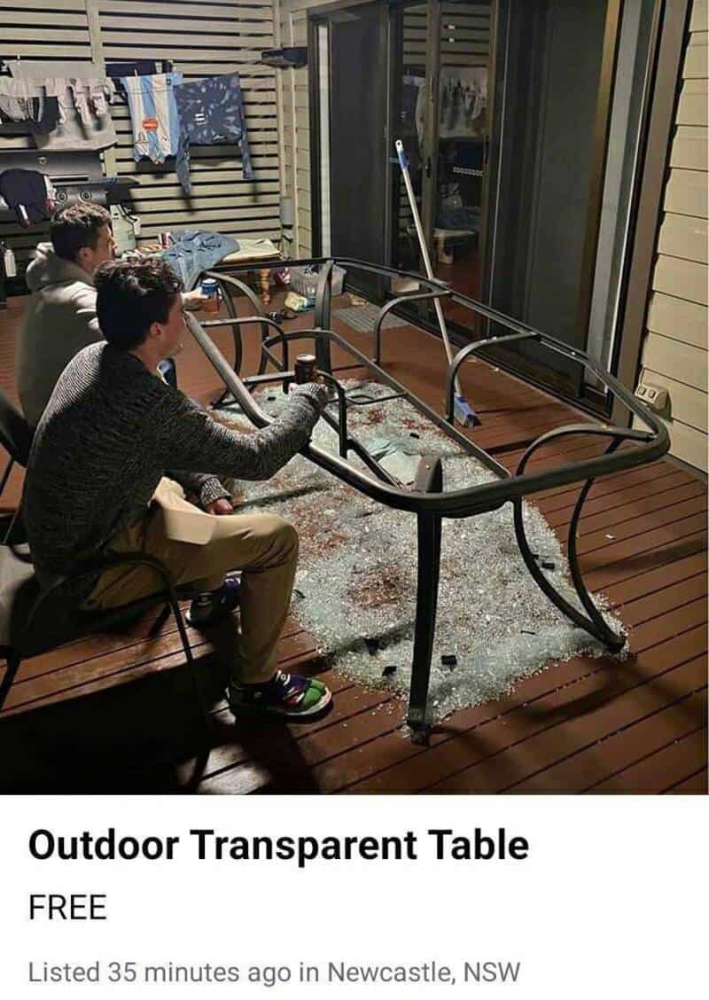 Two boys sit at a broken outdoor transparent table with a glass top and metal frame.