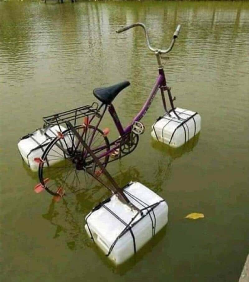 Bicycle with water containers attached, floating in water, tied with ropes.