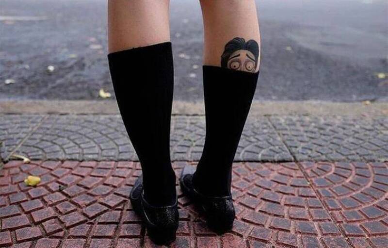 Person with black socks and shoes, revealing a cartoon face tattoo on the leg.