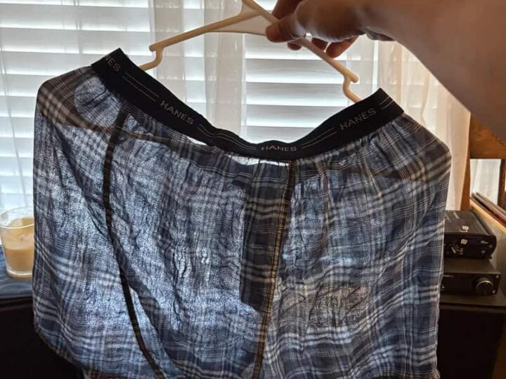 Person holding up a pair of plaid boxer shorts on a hanger.