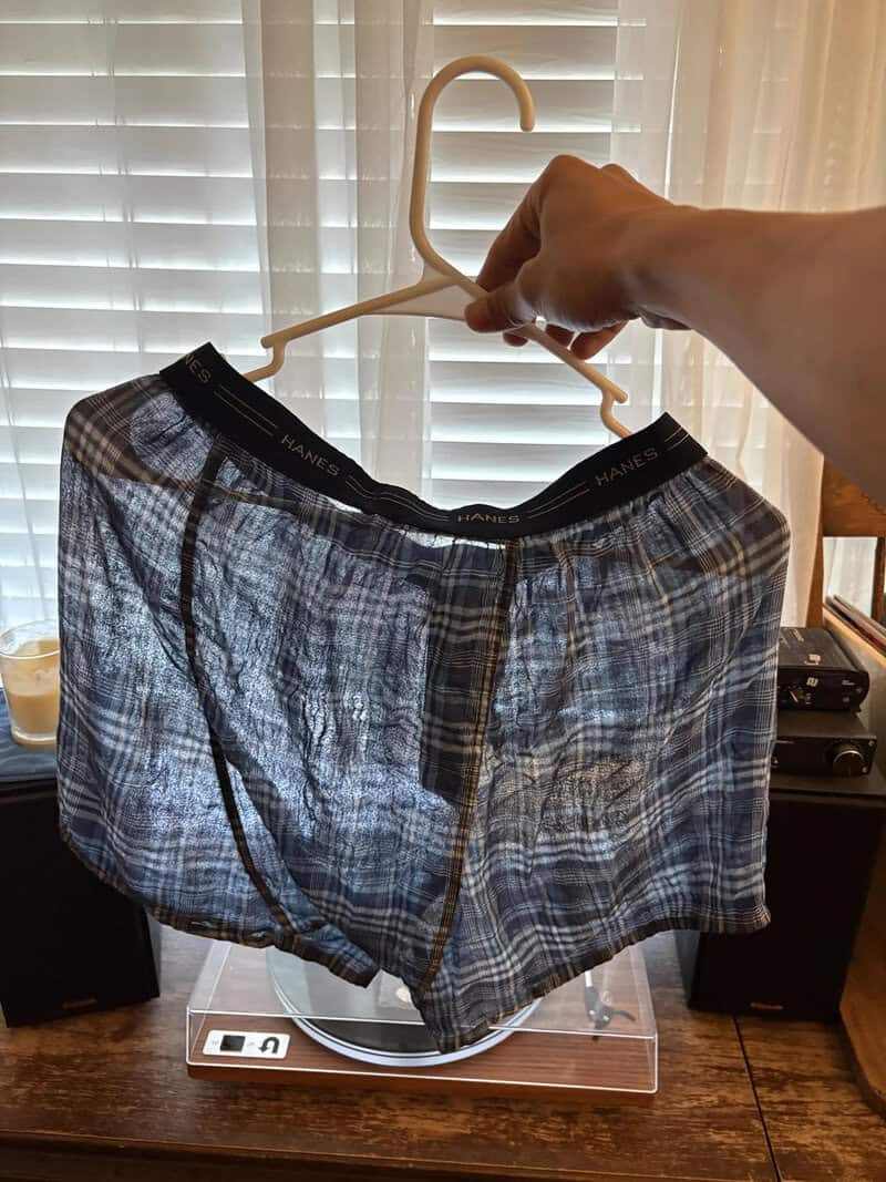 Person holding up a pair of plaid boxer shorts on a hanger.