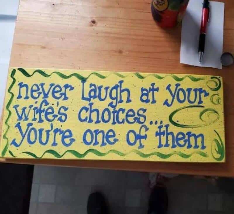 Hand-painted sign says 'never laugh at your wife's choices... You're one of them'.