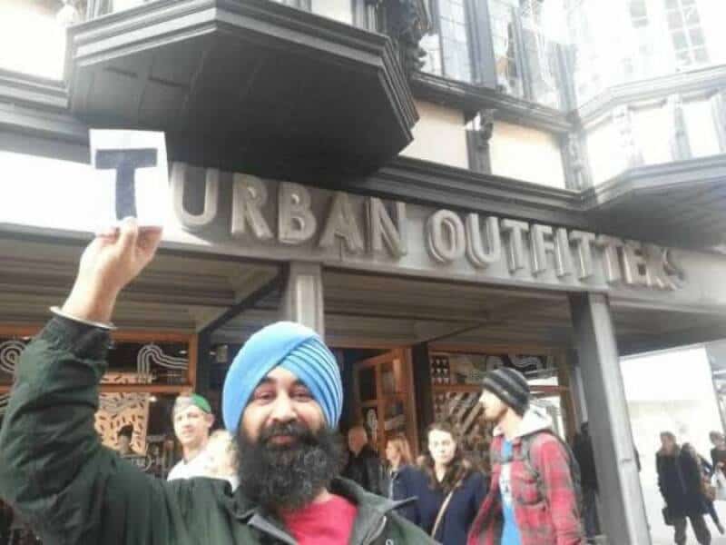 Man with a blue turban holding a sign in front of Urban Outfitters.