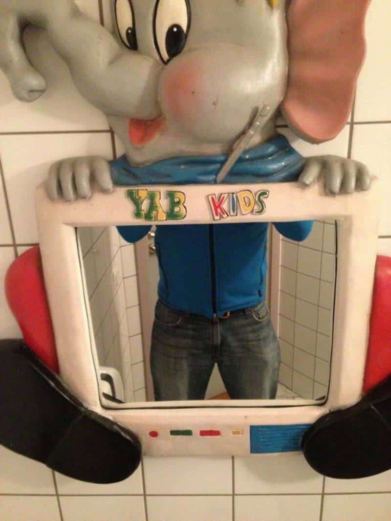 Person holding a mirror with a cartoon character head on top, labeled 'YAB KIDS'.