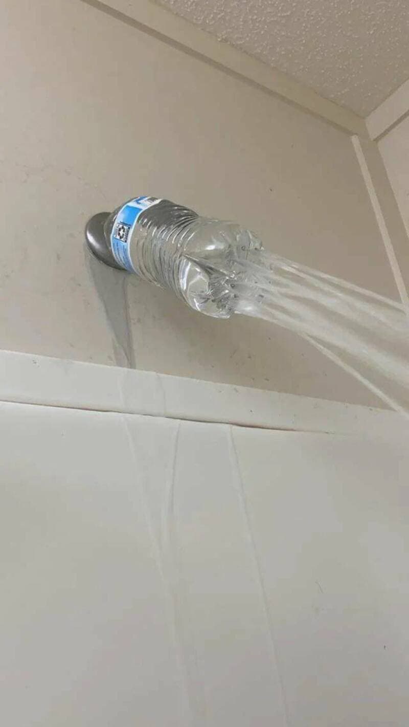 Water flowing from a plastic bottle attached to a wall pipe.