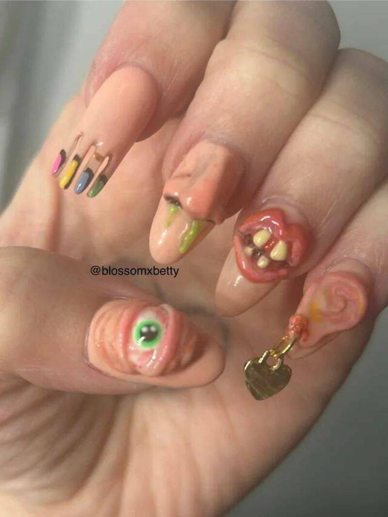 Nail art with colorful, messy designs and a fake eye on one nail, a toothy mouth on another, and a 3.