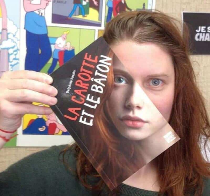 Girl holding a book titled 'La Carpette et le Baton' in front of her face.