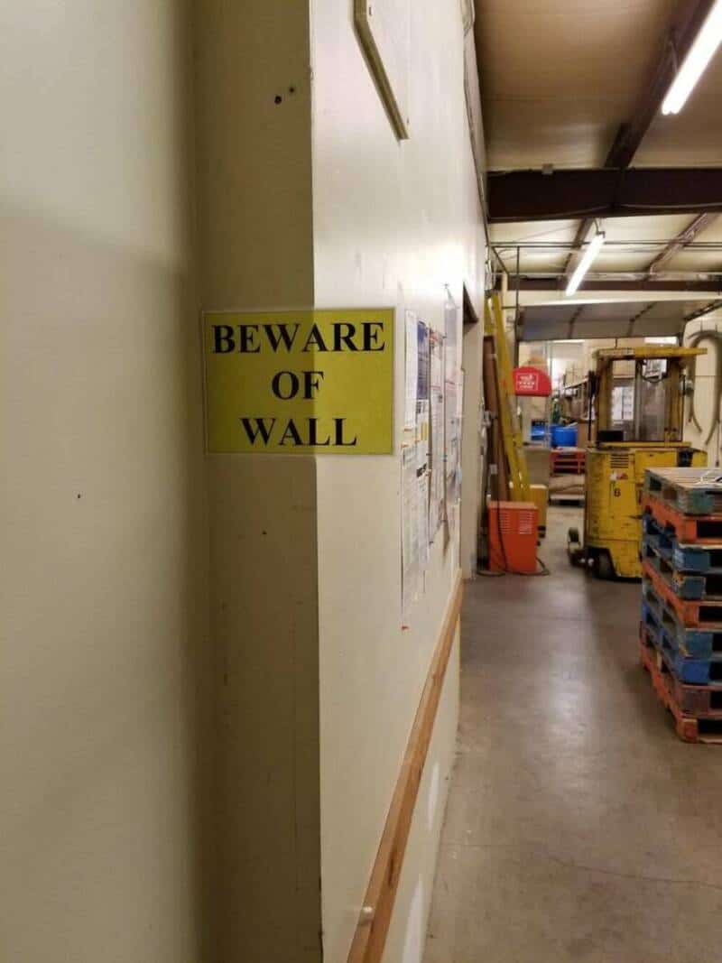 Beware of wall sign in a warehouse with forklifts and pallets.