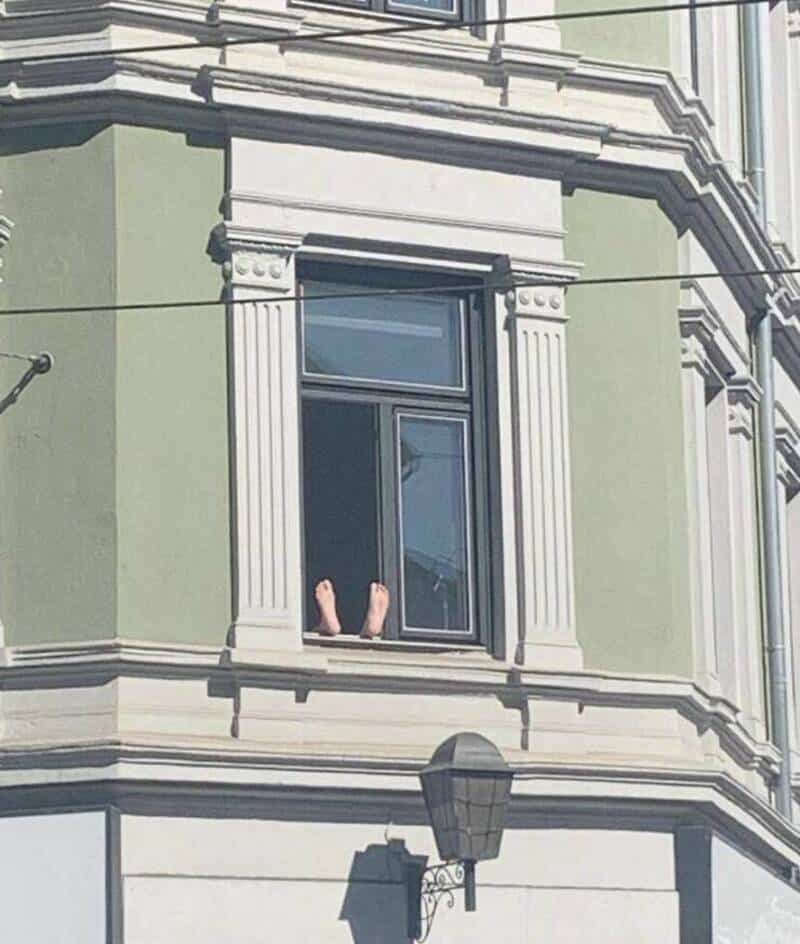Person's feet sticking out of an open window on a green building.