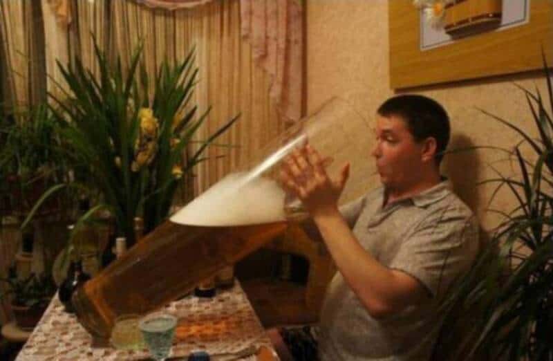 Man holding a giant beer glass at a table in a restaurant.