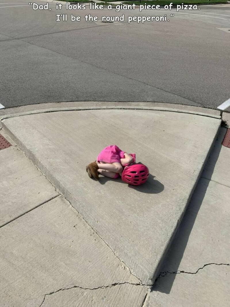 Child lying on sidewalk with pink helmet, looking like a giant pizza piece.