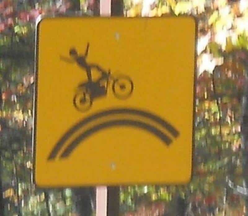 Humorous road sign showing a person falling off a bike over a rainbow.