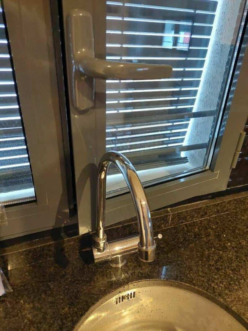 Door handle and lock with a faucet below on a granite countertop.