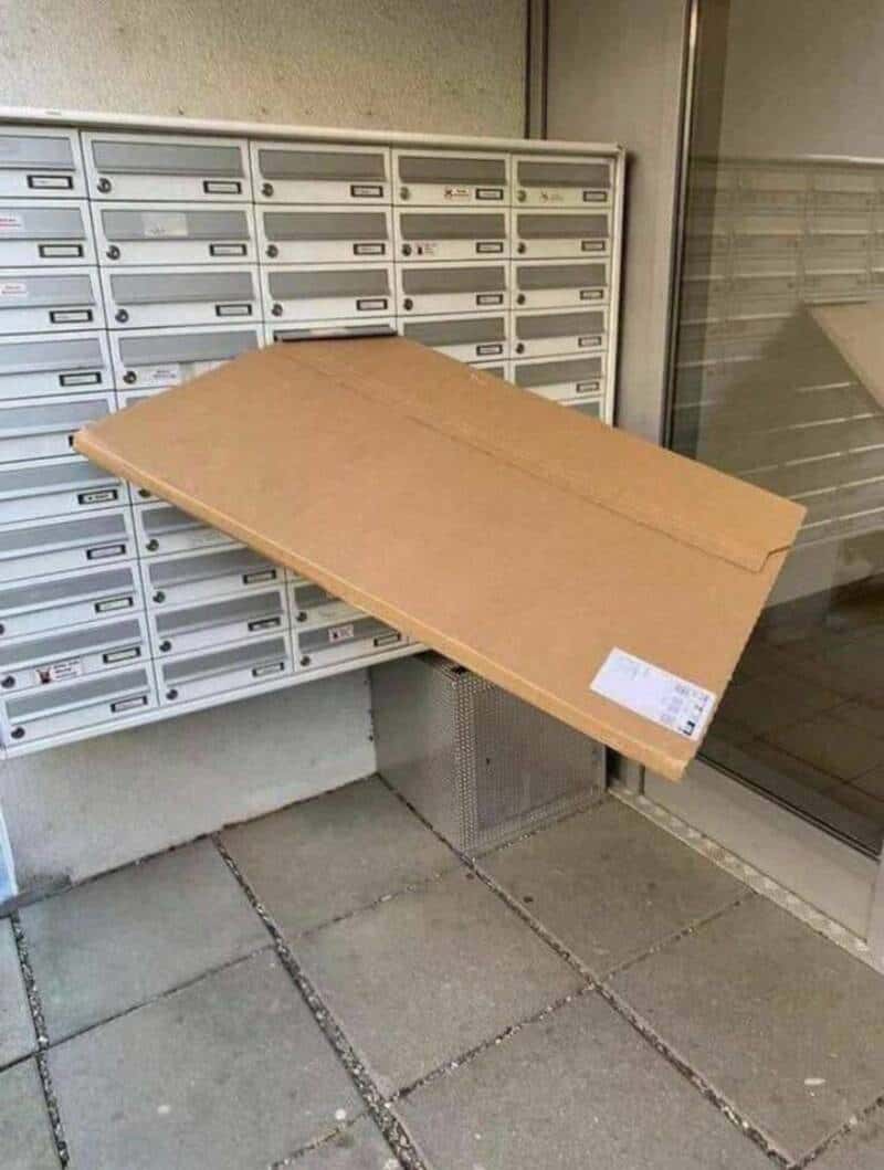 Large cardboard box leaning against mailboxes outside a building.
