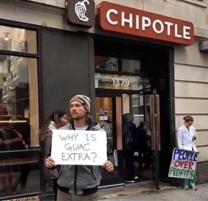 Man holding a sign that says 'WHY IS GUAC EXTRA?' outside Chipotle.