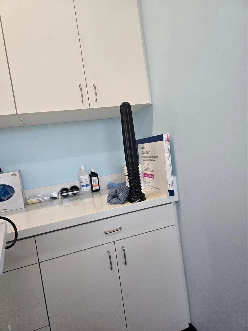A black rubber bat with a textured handle leaning against a wall in a medical room.