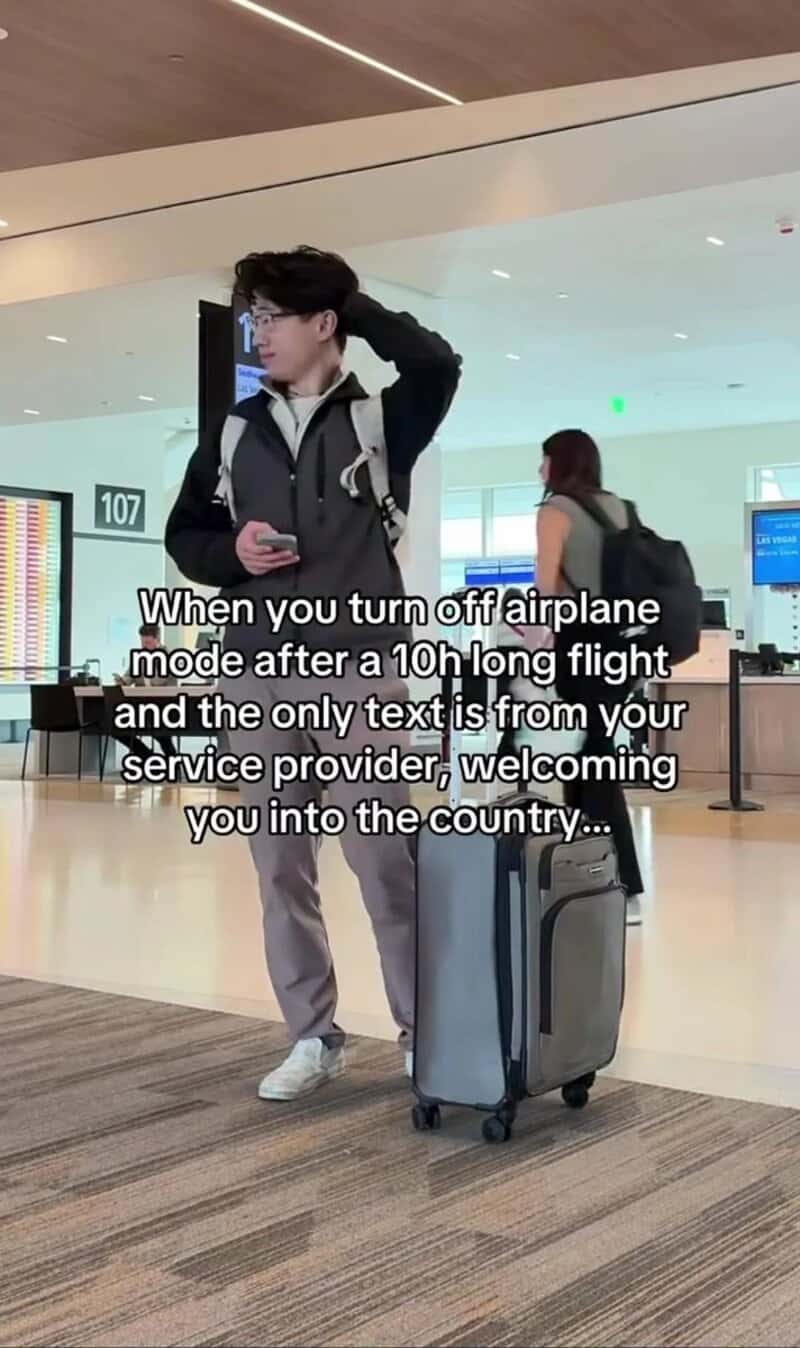 Young man with luggage at airport, looking at phone, after airplane mode is turned off.