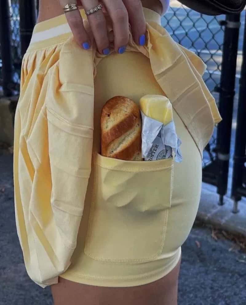 Person in yellow shorts with a pocket holding a bread roll and a butter packet.