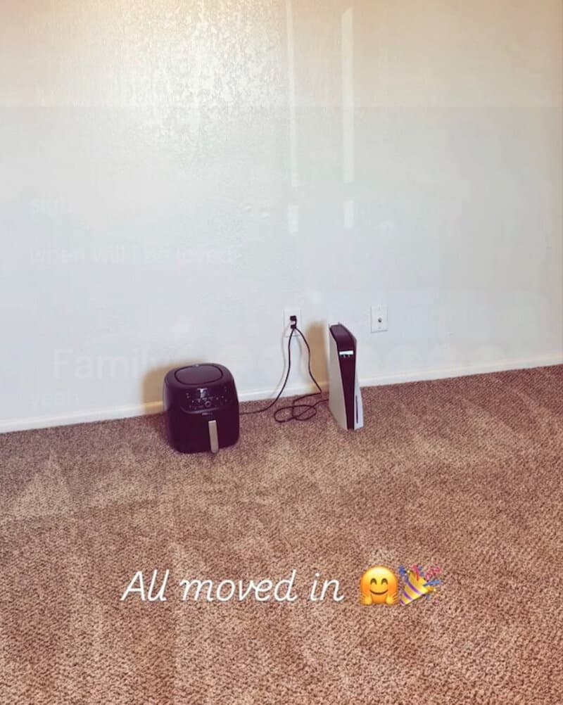 Empty room with a black air purifier and a white tower fan, with text 'All moved in' and a smiling,w.