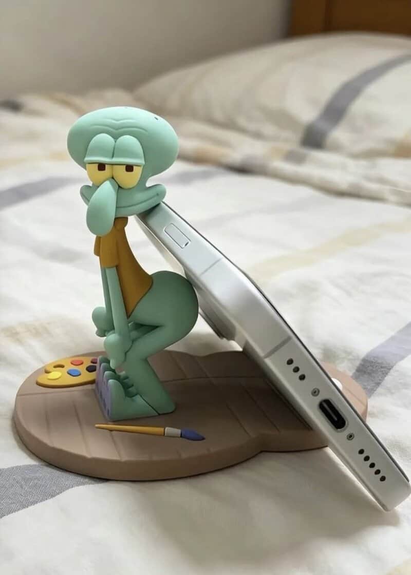 SpongeBob figurine leaning on a phone on a bed.