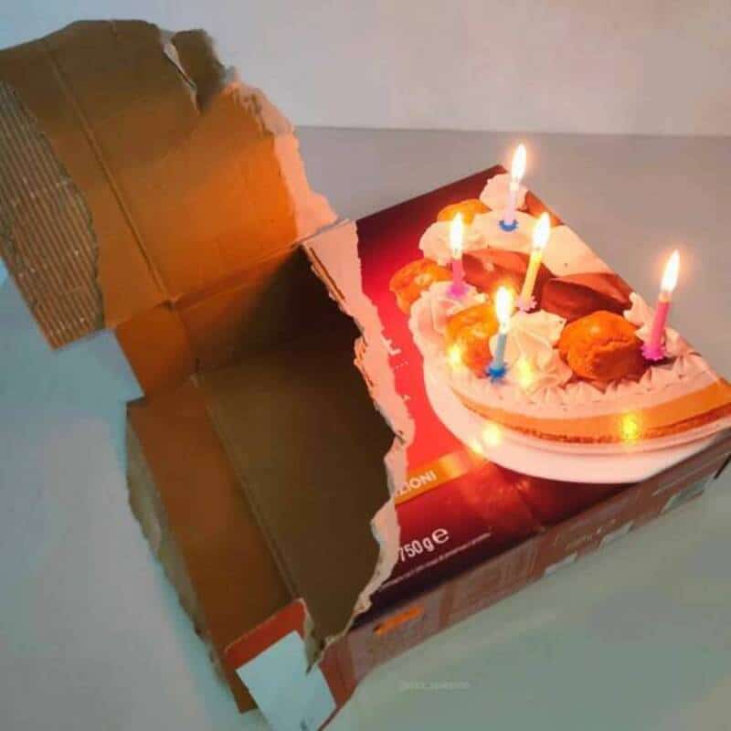 Torn birthday cake box with lit candles and cake inside.