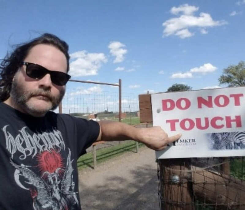 Man with sunglasses pointing at a 'Do Not Touch' sign outside.