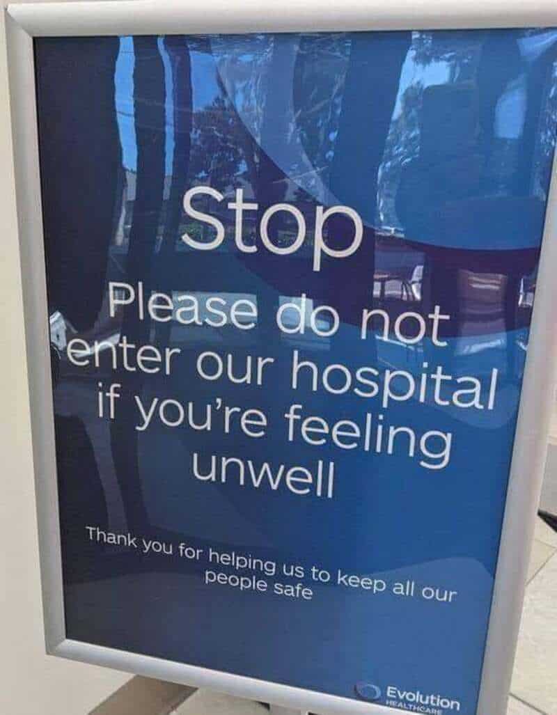 Stop sign at hospital entrance asking not to enter if feeling unwell.