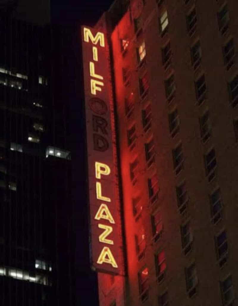 Mildred Plaza sign on a building at night, illuminated in red and yellow.