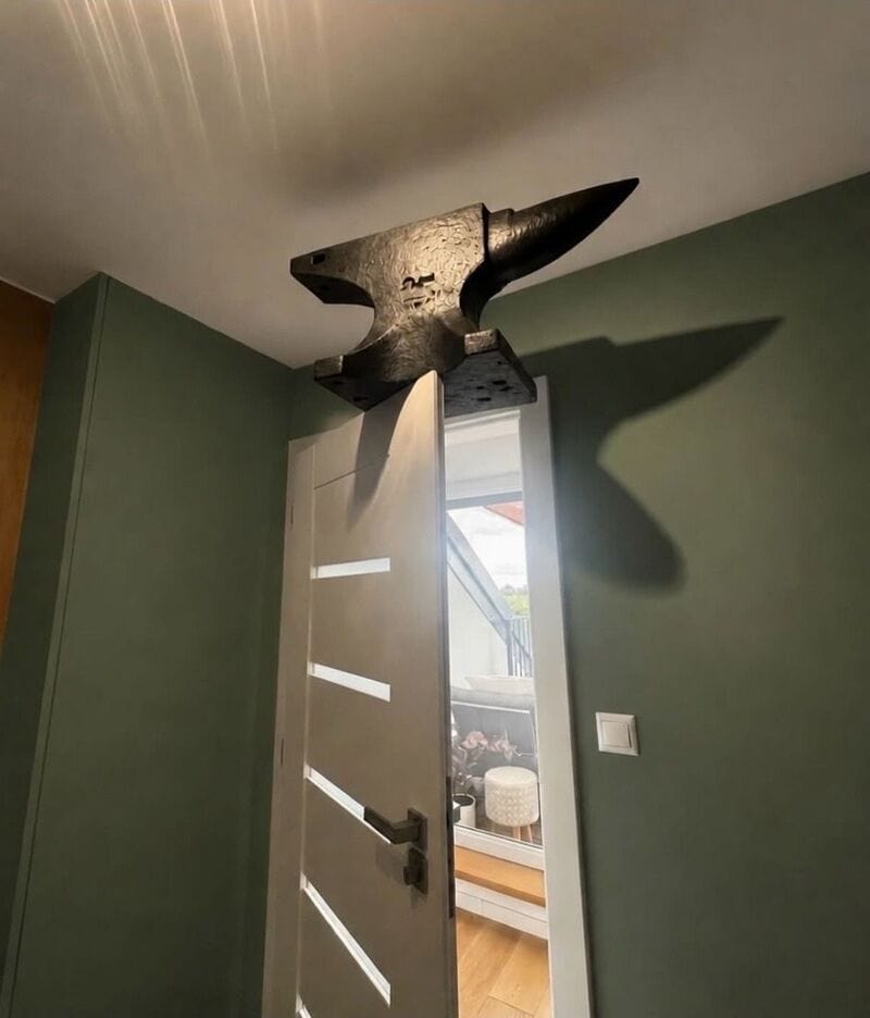 Door with a large hammer-shaped doorstop on top, casting a shadow on the wall.