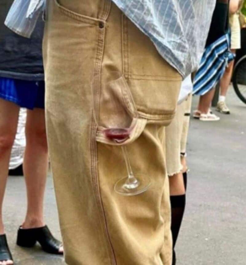 A person wearing beige pants with a wine glass in the pocket.