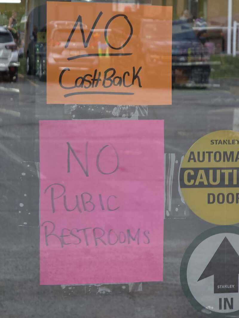 Signs on a door say 'NO Cash Back' and 'NO Public Restrooms' in black and pink ink.