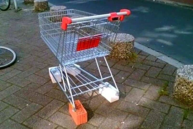 A shopping cart with a brick in the wheel, on a sidewalk near a pool.