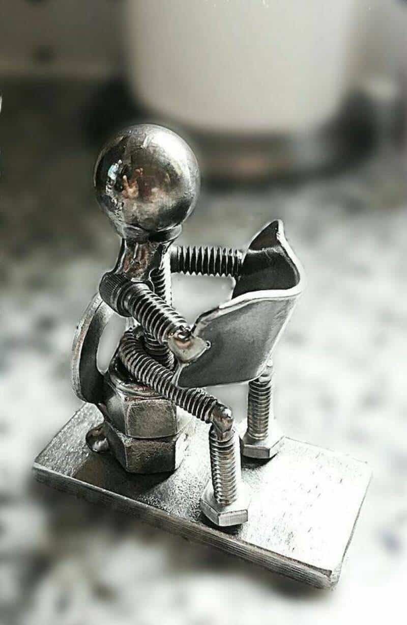 A small metallic robot sitting on a tiny chair, with a shiny round head and coiled limbs.