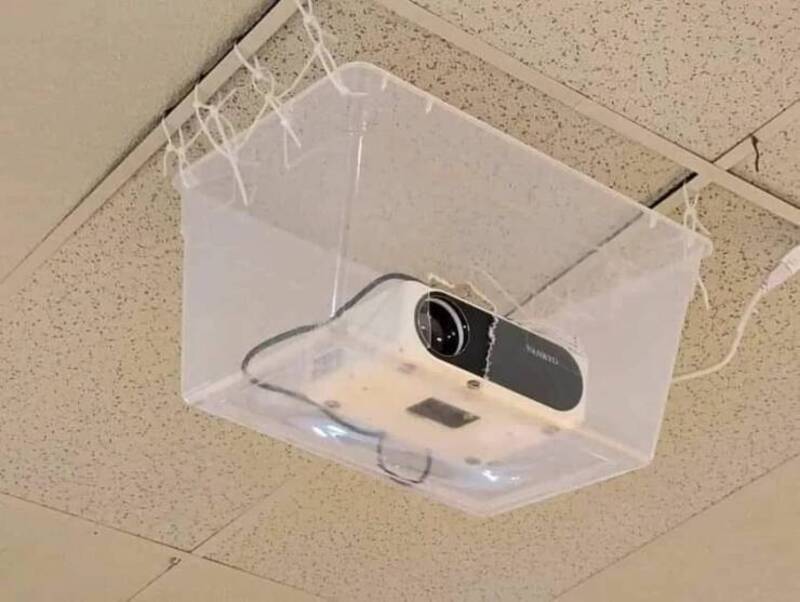 Projector inside a clear plastic box hanging from the ceiling.