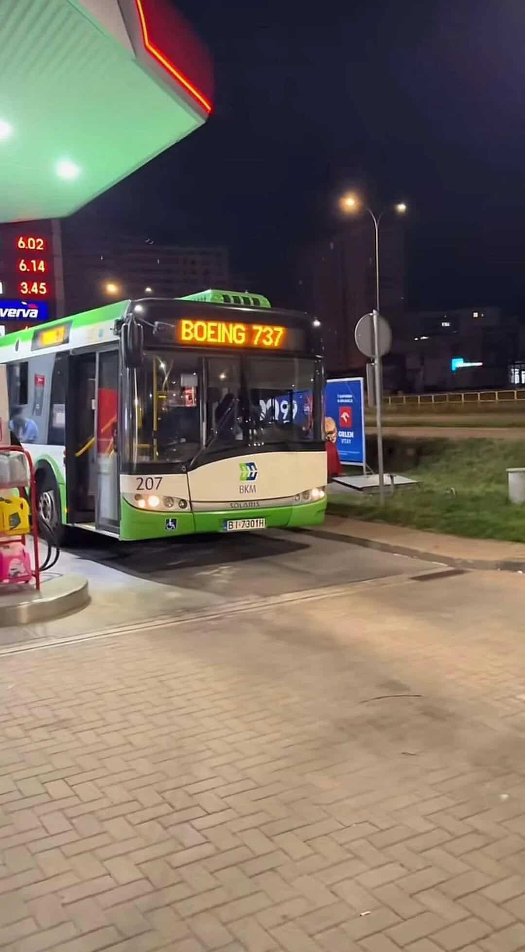 Bus at a gas station with a digital sign showing fuel prices at night.