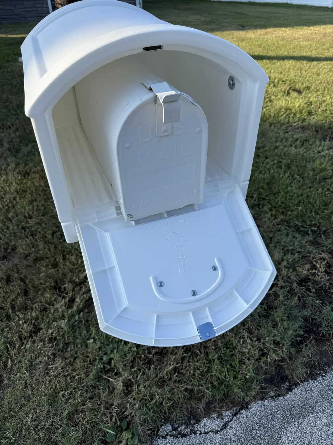 Empty white mailbox with open door on grass, no mail inside.
