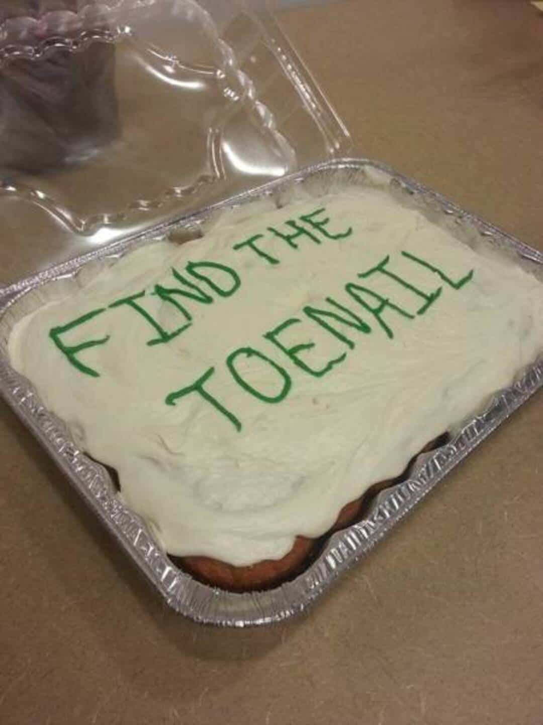 Cake with green writing: 'FIND THE TOENAIL' on white frosting.