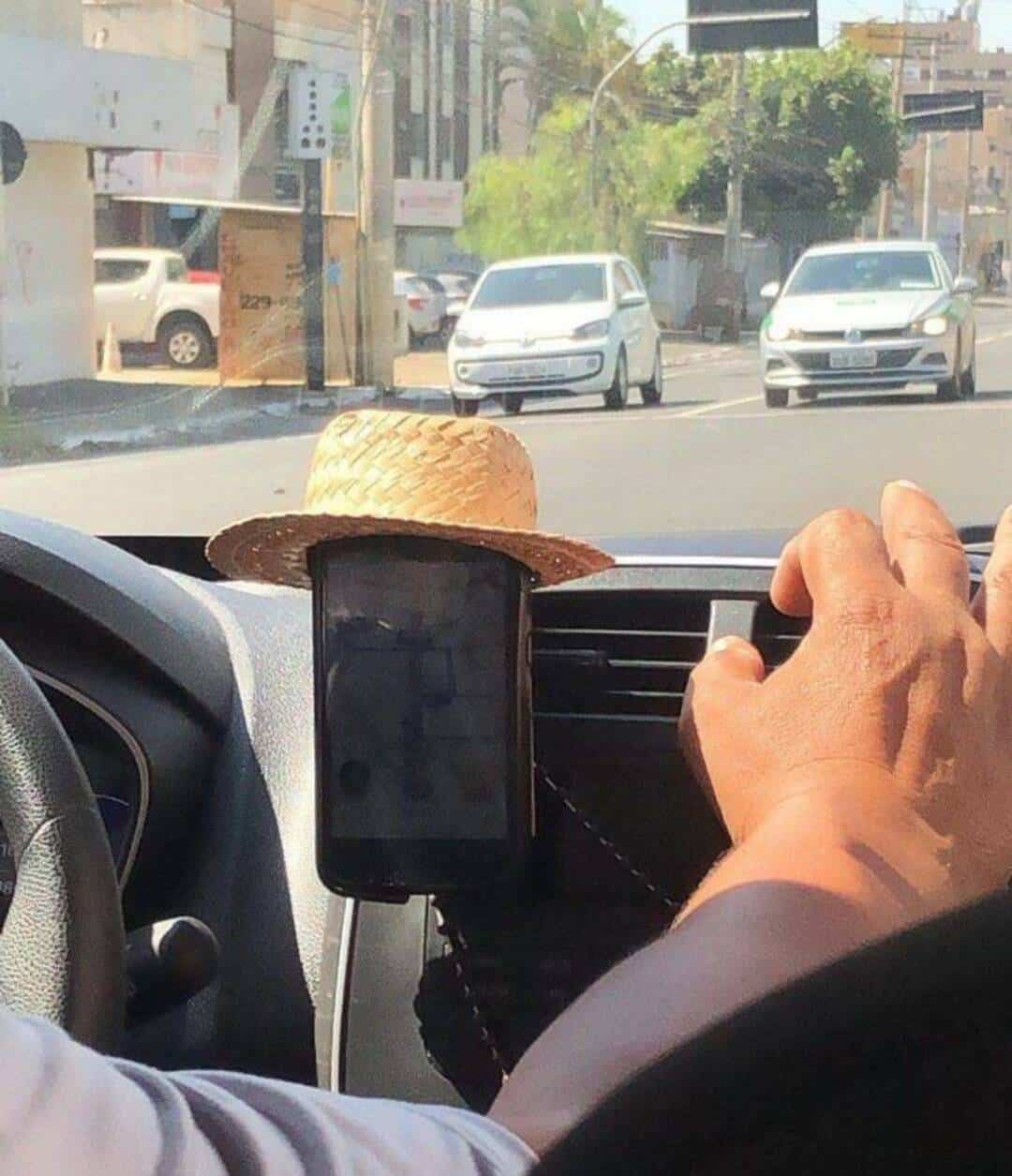 A straw hat on a phone holder in a car, with a hand reaching for the phone.
