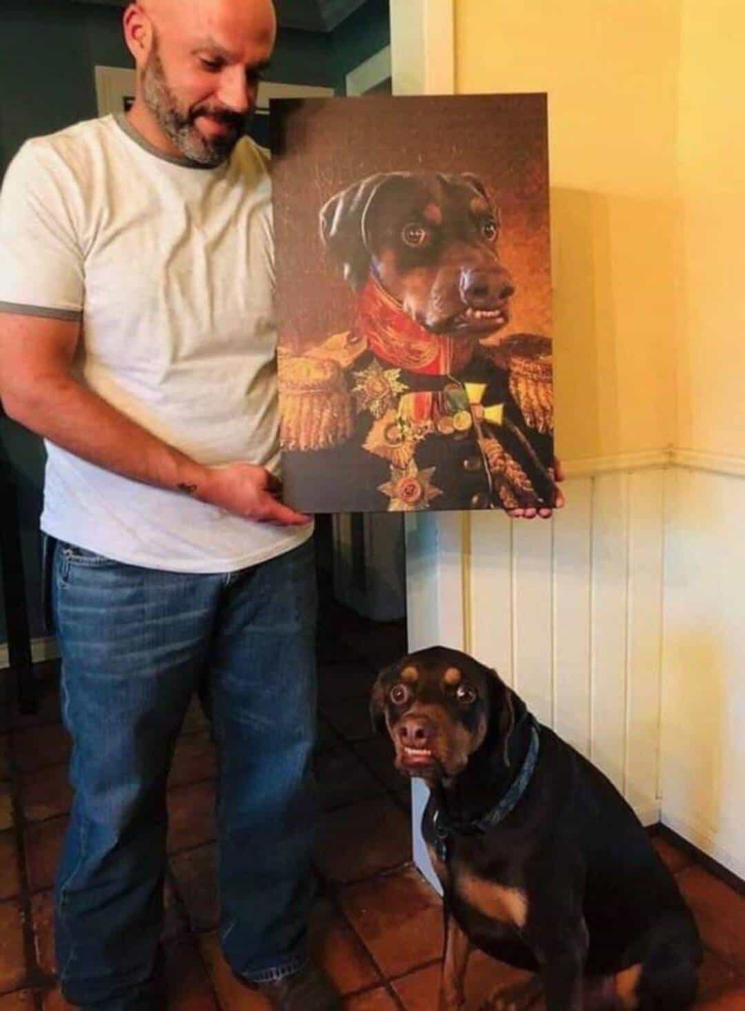 Man holding a painting of a dog dressed as a historical figure with a dog sitting nearby.