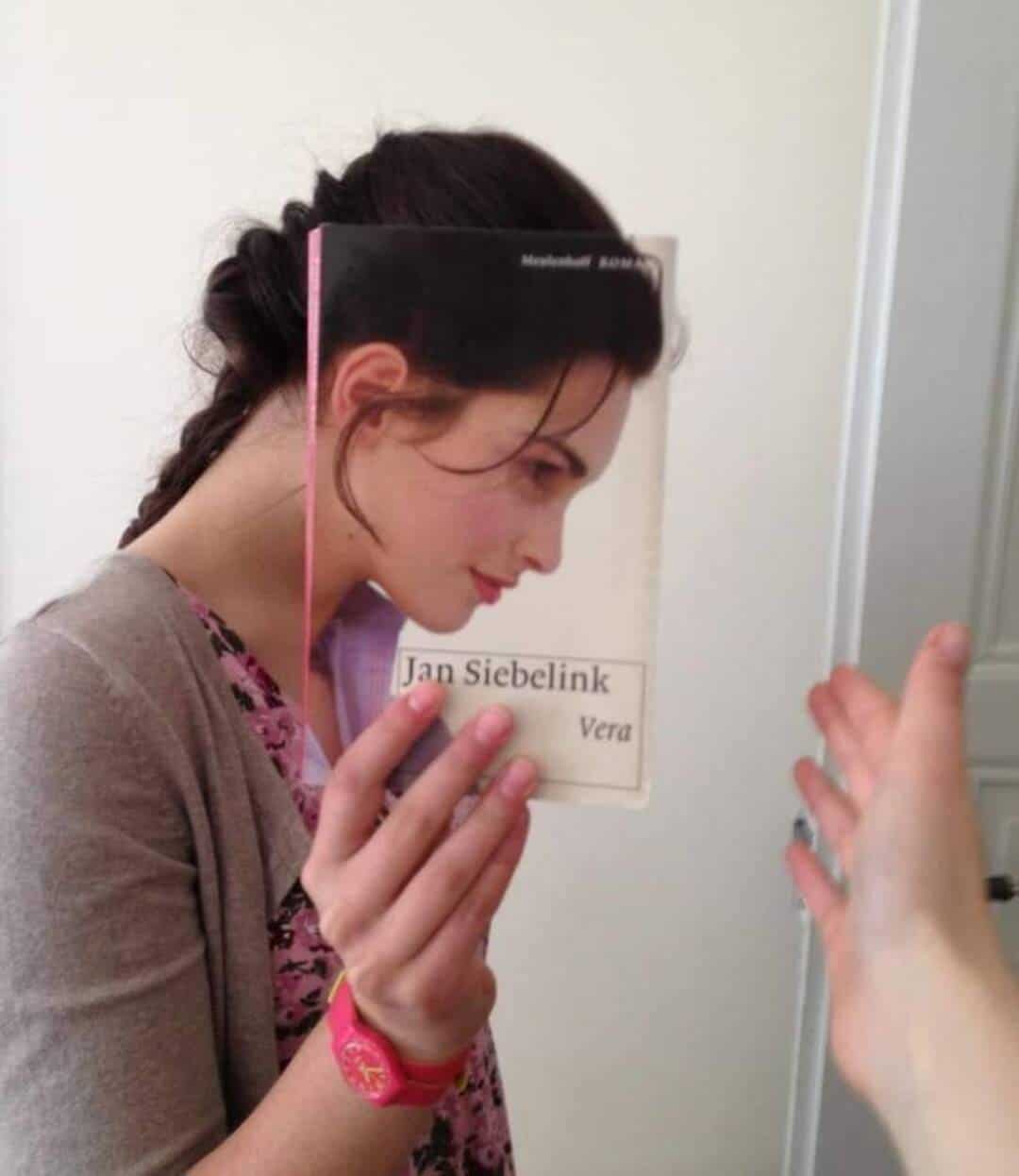 Young woman holding a book titled 'Jan Siebelink Vera' near her face.